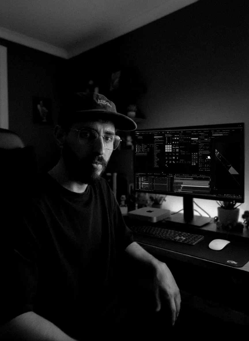 Retrato de Dario Ferez sentado en su escritorio, con gorra y anteojos, junto a un monitor con un software de animación abierto